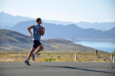 Man jogging on the road beside a lake and mountains